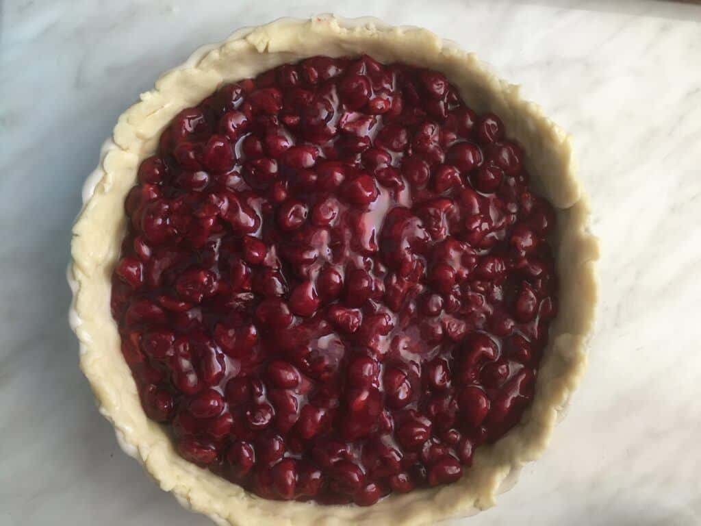 A pie crust in the dish filled with cherries.