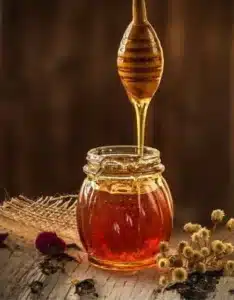 Honey dripping from a honey dipper into a jar of honey.