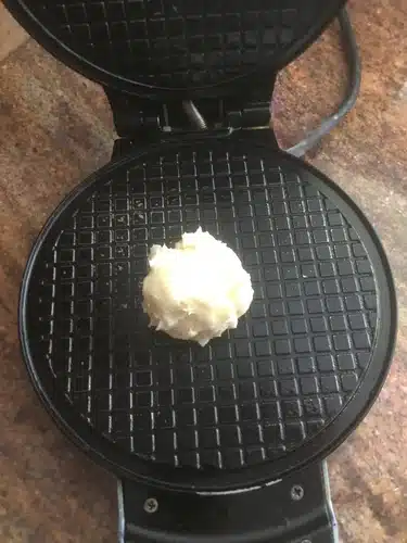 electric thin waffle maker with a spoon of batter and a baked waffle