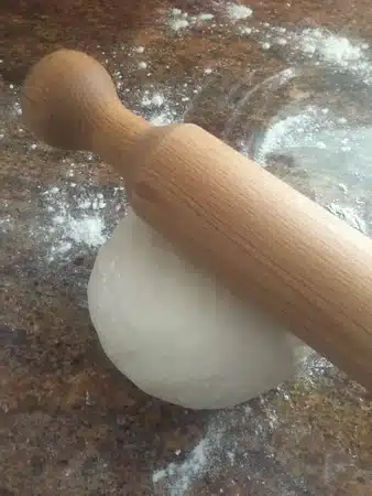 Bread dough and a rolling pin on a floured granite worktop