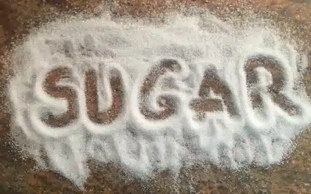 Sugar spilled on a brown surface, with the word sugar written.