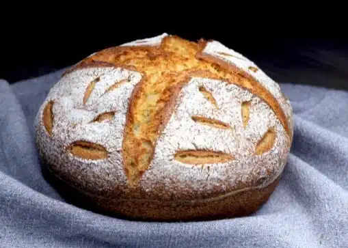 A round sourdough bread decorated with scoring and flour.