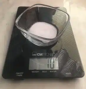 A black digital kitchen scale showing 10 grams, with a glass bowl with salt on the scale.