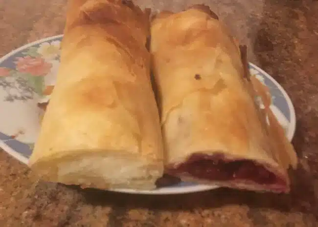 Two strudels on a plate, one filled with cottage cheese, and the other with sour cherries.
