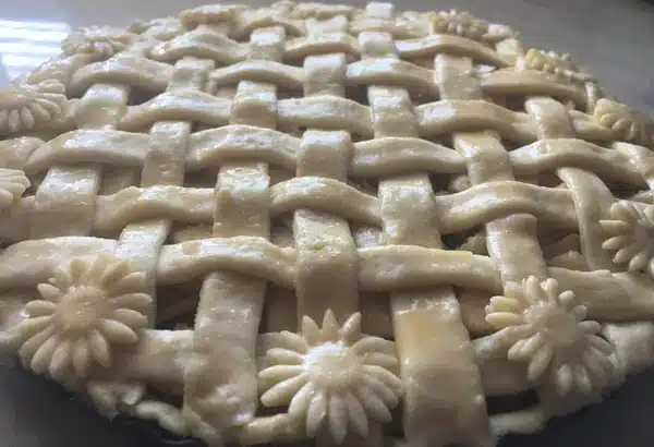 Round apple pie with lattice top and floral decoration before baking.